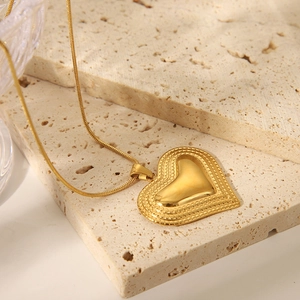 Detailed close-up of golden heart pendant on a sleek snake chain with textured borders