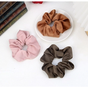 Macro detail of glossy satin fabric scrunchies in pink, coffee, and dark green colors