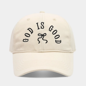 Detailed embroidery of 'GOD IS GOOD' and a bow on a beige cotton baseball cap