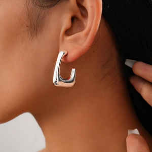 Close-up of a silver geometric rectangular stud earring worn by a model in a high-gloss finish