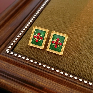 Detail of vintage earrings with green enamel and red gemstones in a gold frame
