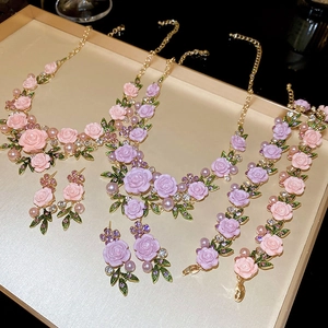 Elegant rose flower jewelry set with pearls and green leaves on a gold tray
