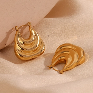 Close-up of gold-plated triple-layered ridged hoop earrings on a neutral stone background
