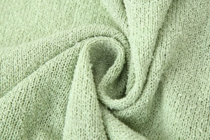 Macro shot of light green knitted fabric showing soft texture and premium bouclé material