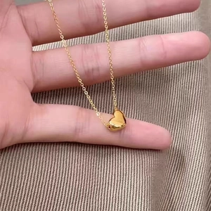 Macro shot of a golden 18K heart pendant necklace held between fingers over fabric