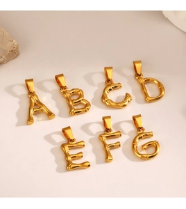Macro detail of golden bamboo textured alphabet pendants A-G on beige background
