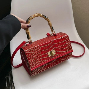 Detail of red crocodile texture handbag with bamboo handle and gold rotating lock clasp