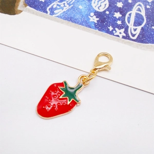 Detail of red and green enamel strawberry charm with golden lobster clasp for bags and shoes