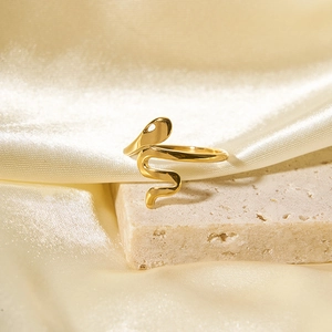 Anello a serpente dorato lucido su pietra chiara con elegante sfondo in seta