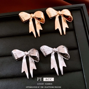 Elegant bow stud earrings in gold and silver finish displayed on a black jewelry tray