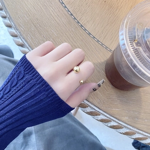 Close-up of a minimalist gold ball open ring worn on a finger in a café setting