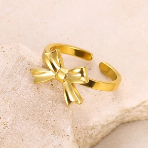 Close-up of golden bow-shaped open ring on a textured stone surface with metallic luster