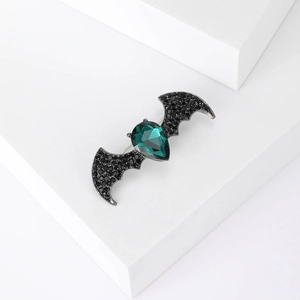 Gothic bat brooch with green crystal and black rhinestones on a white pedestal