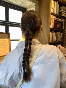 Rear view of a model wearing a black bow hair clip on braided hair in a cozy setting