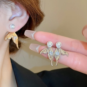 Detail view of gold and silver mermaid tail earrings with heart zircon and white pearl