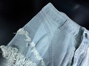 Dettaglio di pantaloncini di denim azzurro a vita alta con strappi decorativi