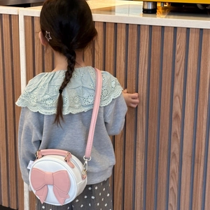 Cute round white PU leather crossbody bag with pink bow worn by a child model in winter