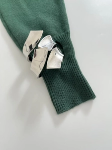 Close-up of a wide silver sculptural metal cuff worn over dark green knit sleeves