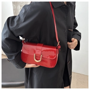 Detail of red patent leather shoulder bag with gold horseshoe buckle on model