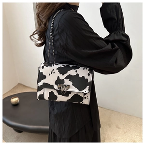 Detalle de bolso bandolera con estampado de vaca, cadena y cierre de solapa en modelo