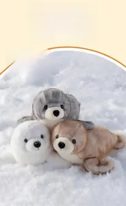 Tre peluche a forma di foca in grigio, bianco e marrone sulla neve soffice