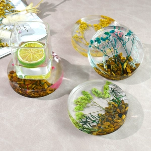 Detail of round resin coaster featuring dried flowers and crushed stones with a glass cup