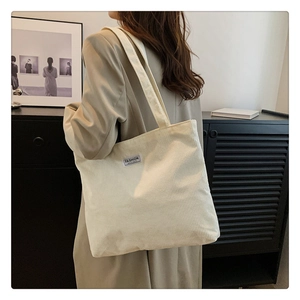 Detailed side view of a cream corduroy tote bag with a minimalist fashion label strap