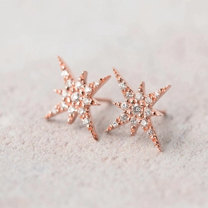 Pendientes de estrella en oro rosa con circonitas brillantes sobre un fondo gris liso