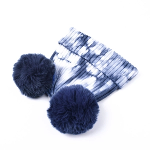 Dettaglio del berretto in maglia tie-dye blu e bianco con due pompon in ecopelliccia