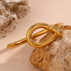 Polished 18K gold teardrop knotted bangle displayed on natural stones backdrop