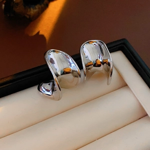 Close-up of sculptural C-shaped silver metal earrings in a beige jewelry box