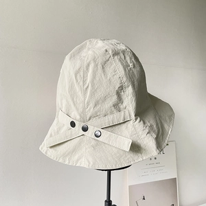 Detail of beige nylon sun hat with cross strap and three black decorative buttons