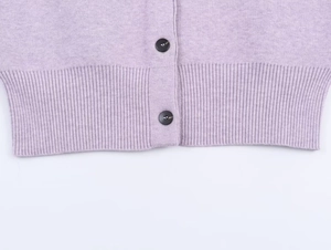 Macro detail of lavender knit cardigan featuring ribbed hem and dark tortoise shell button