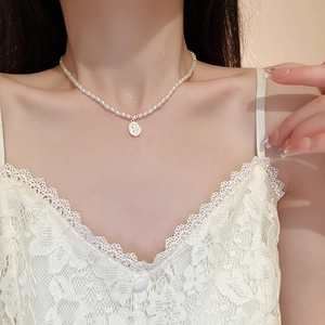 Detail of elegant pearl necklace featuring a golden tulip pendant on white lace dress