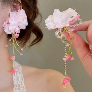 Detailed macro view of large pink fabric flower tassel earrings with golden chains
