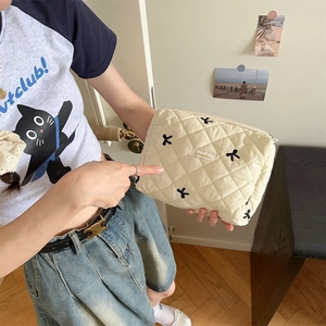 Detailed view of cream quilted makeup bag with black bow embroidery held by hands