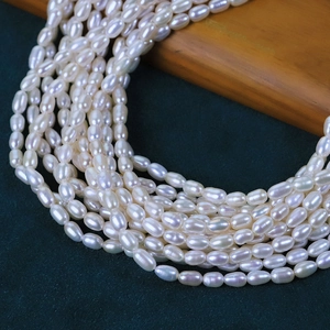 Lustrous 4mm white oval freshwater pearls on dark green and wood background for jewelry DIY