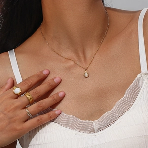 Close-up of model wearing a gold water drop opal necklace and stacked textured gold rings