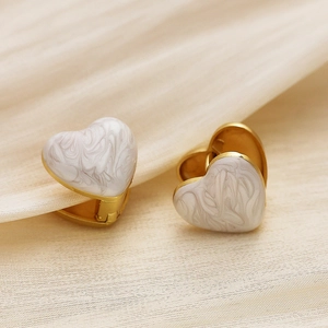 Détail de boucles d'oreilles cœur en émail marbré blanc sur une base dorée