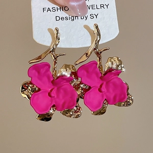 Macro shot of rose red matte flower earrings with golden branch accents on white card