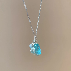 Detail of light blue raw stone pendant with silver wire wrap and small floral accents