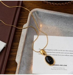 Close-up of a gold oval pendant necklace with a black stone on an aesthetic card