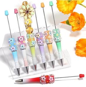 Detail of gradient DIY beaded pens with floral charms and fuzzy ball on acrylic stand