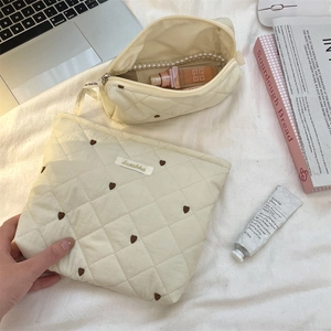 Flat lay of cream quilted toiletry bags with brown heart embroidery on a white bed