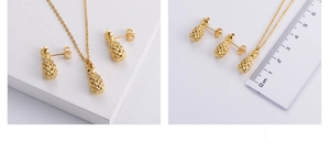 Macro detail of gold pineapple jewelry set with measurements on a white textured background