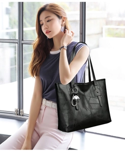 Detailed view of large black PU leather tote bag with panda pendant in indoor setting