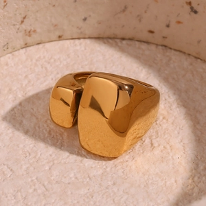 Détail d'une bague géométrique plaquée or 18K dans un récipient en céramique beige et lumière douce