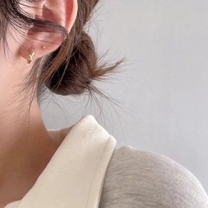 Close-up of minimalist gold twisted knot earrings and stud worn by a model