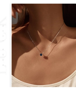 Close-up of a silver necklace featuring a round sapphire blue pendant on a female model