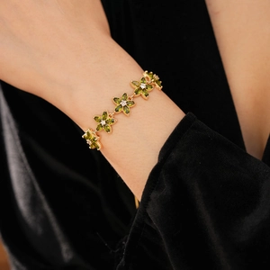 Detail eines Armbands mit olivgrünen Blütenblättern und goldener Kette auf schwarzem Samt